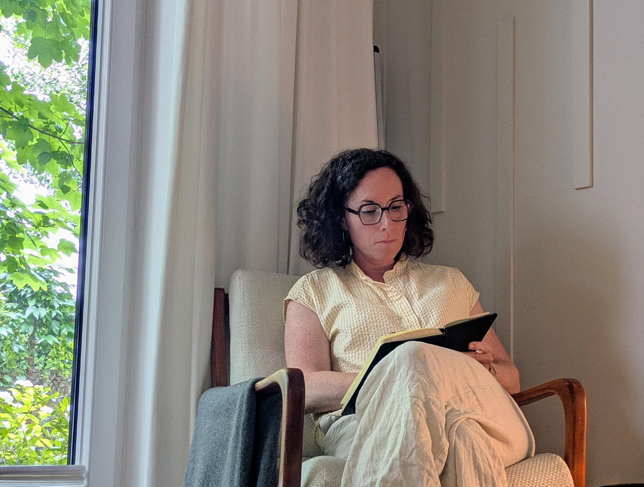 Frau liest konzentriert in einem Sessel am Fenster – ruhige Präsenz und Reflexion als Stärke introvertierter Führungskräfte